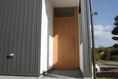 アトリエ入口は木製ドア。白の外壁とグレーの外観のコントラスト。スイス漆喰を使用。